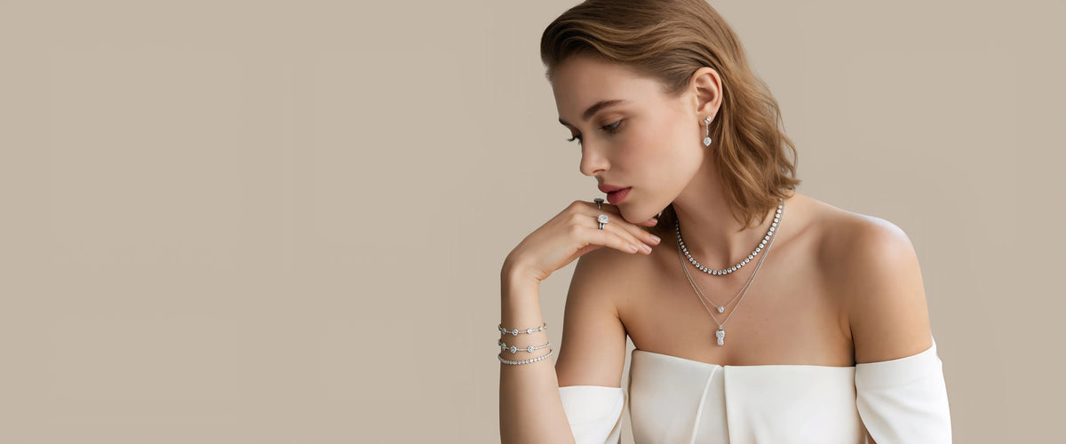 A woman in an ivory off-the-shoulder outfit wearing diamond drop earrings, layered diamond necklaces, rings and bracelets.
